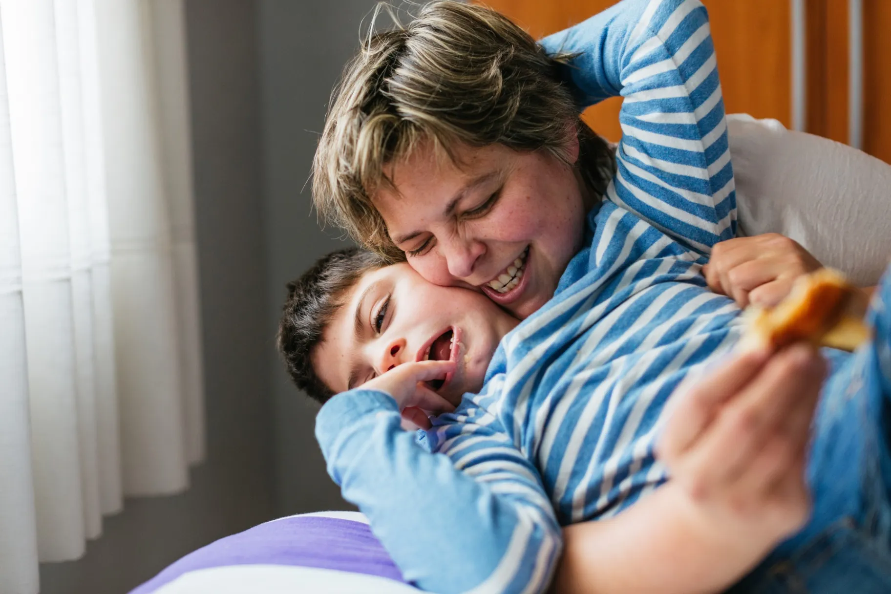 Mother embracing and tickling her son with disability with affection